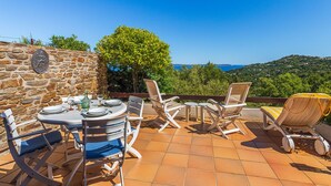 Une terrasse extérieure avec un mur en pierre, une table ronde dressée pour le repas et des chaises longues.
