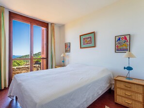 Ein Schlafzimmer mit Bett, Nachttisch, Lampe und Blick ins Freie.