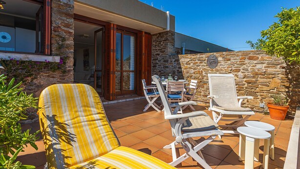 Une terrasse avec des meubles d’extérieur, un mur en pierre et une vue sur l’intérieur.