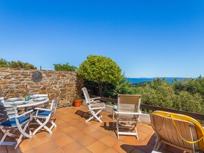 Eine Terrasse mit einer Steinmauer, einem Tisch gedeckt mit Geschirr und Gläsern, und Blick auf das Meer.