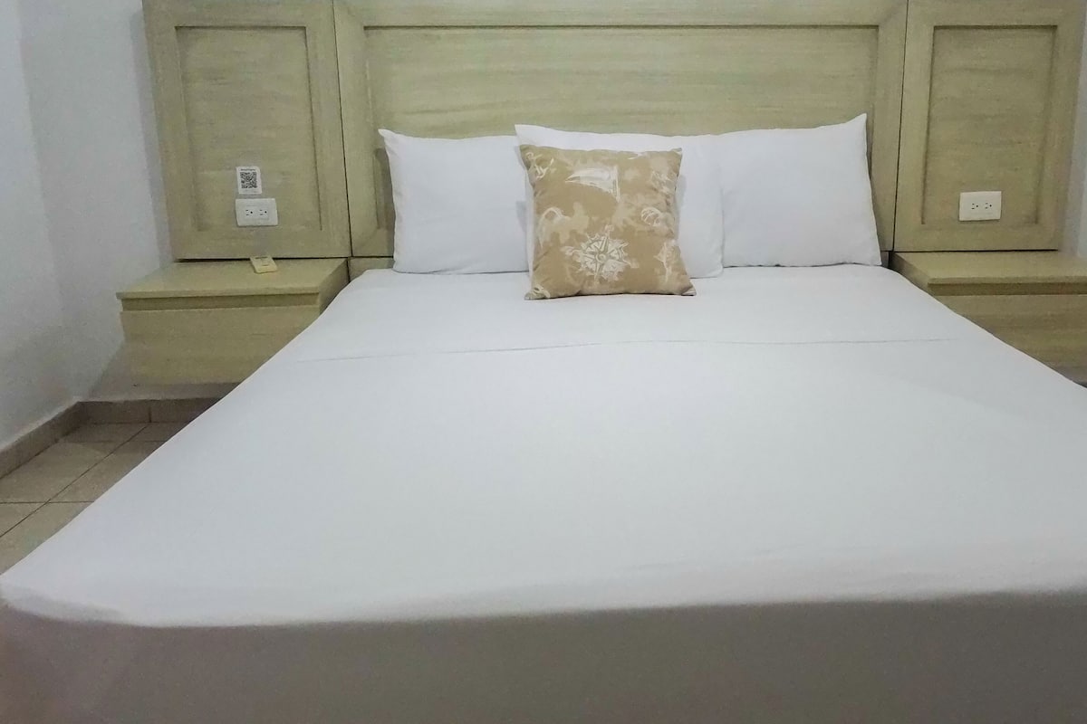Un letto rifatto con lenzuola bianche e un cuscino decorato, affiancato da due comodini dal design semplice.