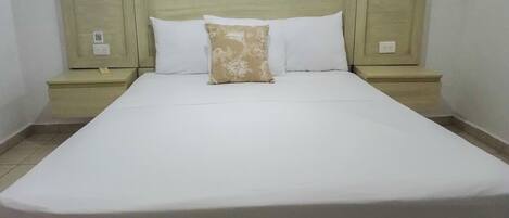 A neatly made bed with white linens and a single patterned pillow, flanked by two nightstands with a simple design.