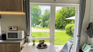 A compact kitchen with a microwave, a small table with a coffee maker, and a view of a garden through a glass door.