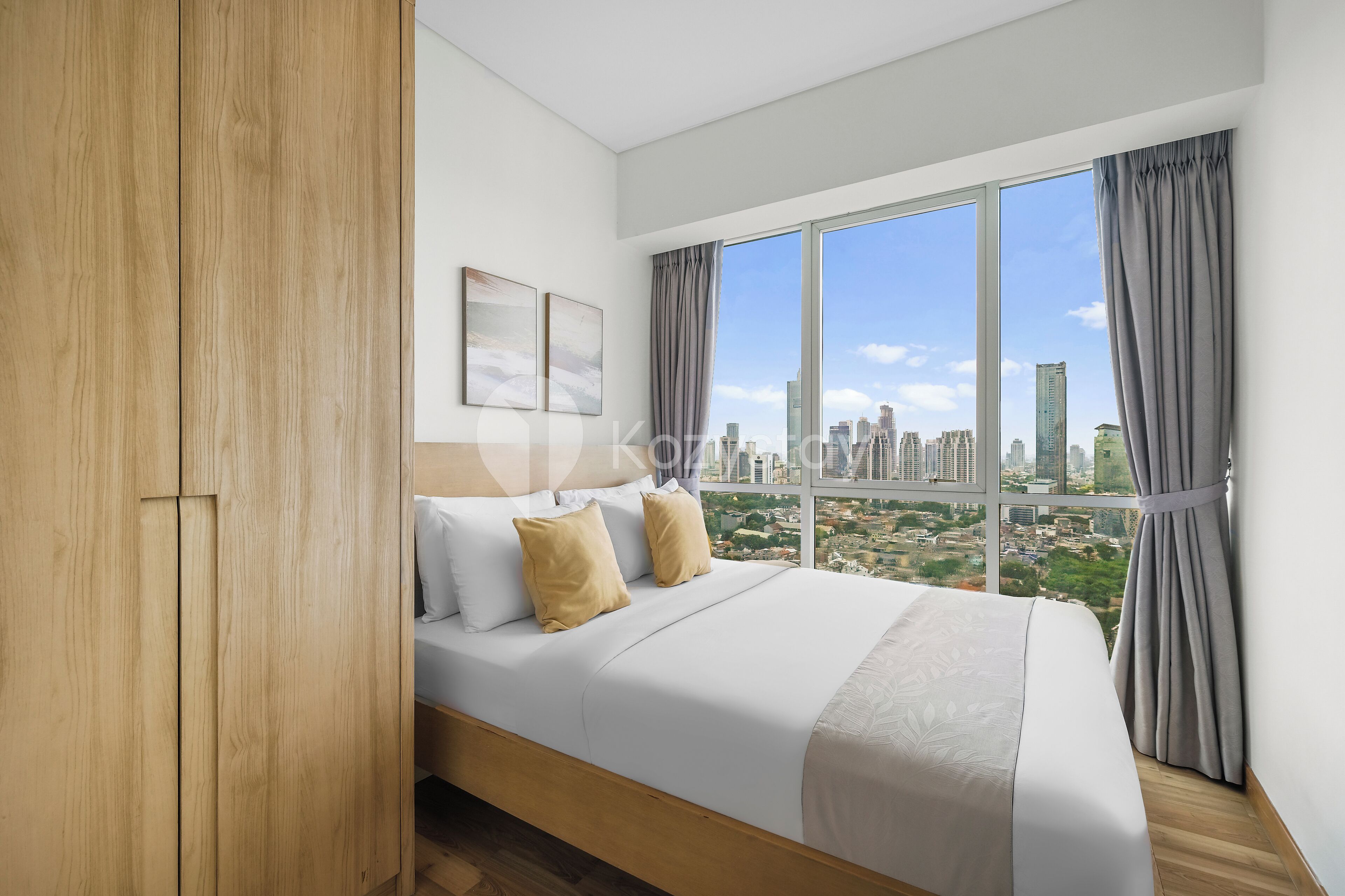A modern hotel room with a large bed, wooden wardrobe, and a city view through large windows.