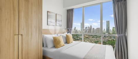 A modern hotel room with a large bed, wooden wardrobe, and a city view through large windows.