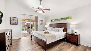 Une chambre avec un lit, des tables de chevet, un ventilateur de plafond et une vue sur une piscine.