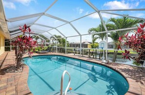 An indoor swimming pool with a clear view of the surrounding area, including a basketball hoop and palm trees. - Sand By Me | Heated Pool | Gulf Access & Dock | Near Pelican Sports (Cape Coral)