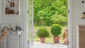 Une porte ouverte donnant sur un jardin où se trouvent des plantes en pot et une bibliothèque.