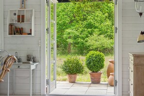 An open door leading to a garden with potted plants and a bookshelf.