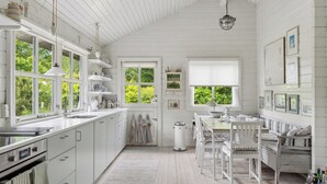 Une cuisine spacieuse avec des meubles blancs, un coin repas doté d’une banquette et de grandes fenêtres offrant une vue sur la verdure.