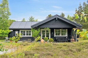 Ein schwarzes Haus mit geneigtem Dach, einer Veranda mit einer Bank und Kübelpflanzen.