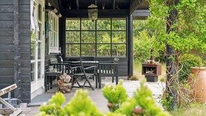 Une véranda en bois avec une table et des chaises, un luminaire suspendu et une vue sur la verdure environnante.