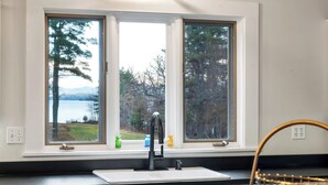 Una cocina con un lavaplatos doble, dos ventanas y vistas a árboles y un lago.