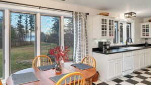 Una cocina con ventanas amplias, una mesa de comedor con sillas y armarios blancos.