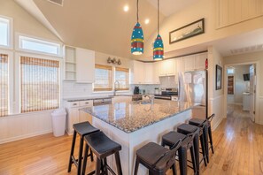 A kitchen with a central island, bar stools, white cabinets, and pendant lights. - Patriot's Place - Corolla, Ocean Sands, 180 Yds to Beach, Pool, Hot Tub, Pool Table, Pets OK (Corolla)