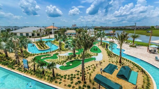 A golf course with a pool, palm trees, and a view of the city skyline. - Spacious 5-bedroom 4-bath townhome, private pool and Resort, near Disney (Kissimmee)