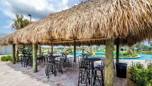 An outdoor patio area with thatched umbrellas, tables, and chairs. - Spacious 5-bedroom 4-bath townhome, private pool and Resort, near Disney (Kissimmee)