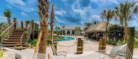 Ein Poolbereich eines Resorts mit einer Hängematte, Palmen und einer Struktur mit Reetdach.