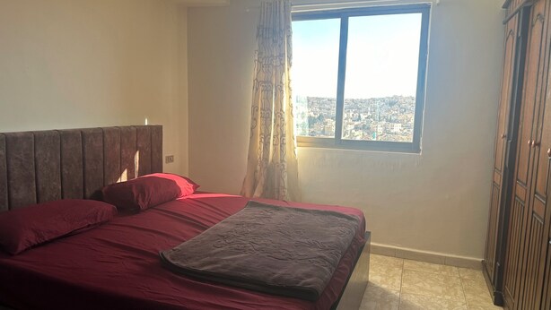 A bedroom with a bed, a window with a view of a cityscape, and a wardrobe.