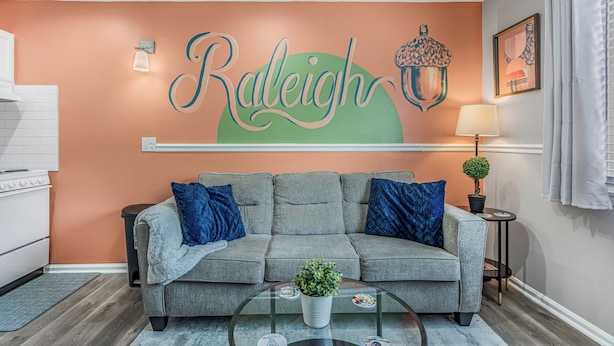 Un salon comprenant un canapé, une table basse en verre et un mur sur lequel est peint le mot « Raleigh ».