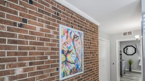 Un couloir avec un mur en briques et un tableau abstrait aux couleurs vives.