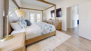 Un dormitorio con cama con dosel, una lámpara de noche, un escritorio y un televisor.