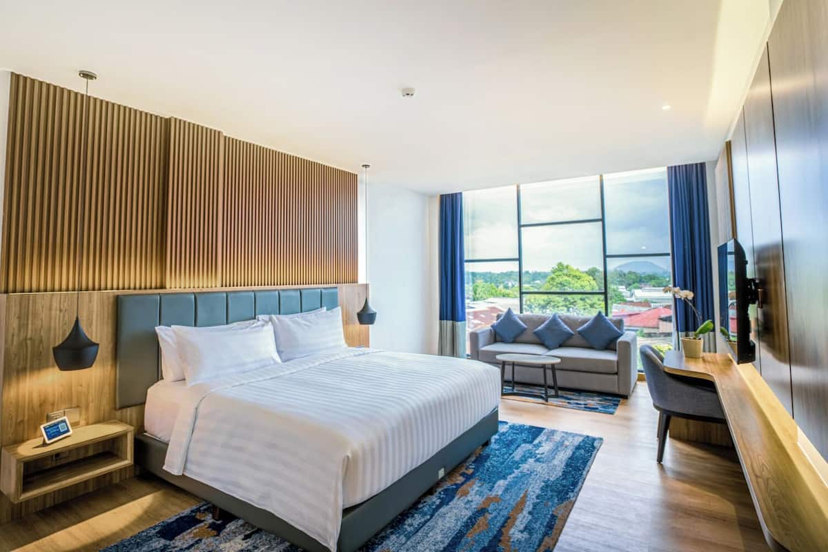 Una habitación de hotel moderna con una cama grande, un sofá, un escritorio y vistas a la ciudad.