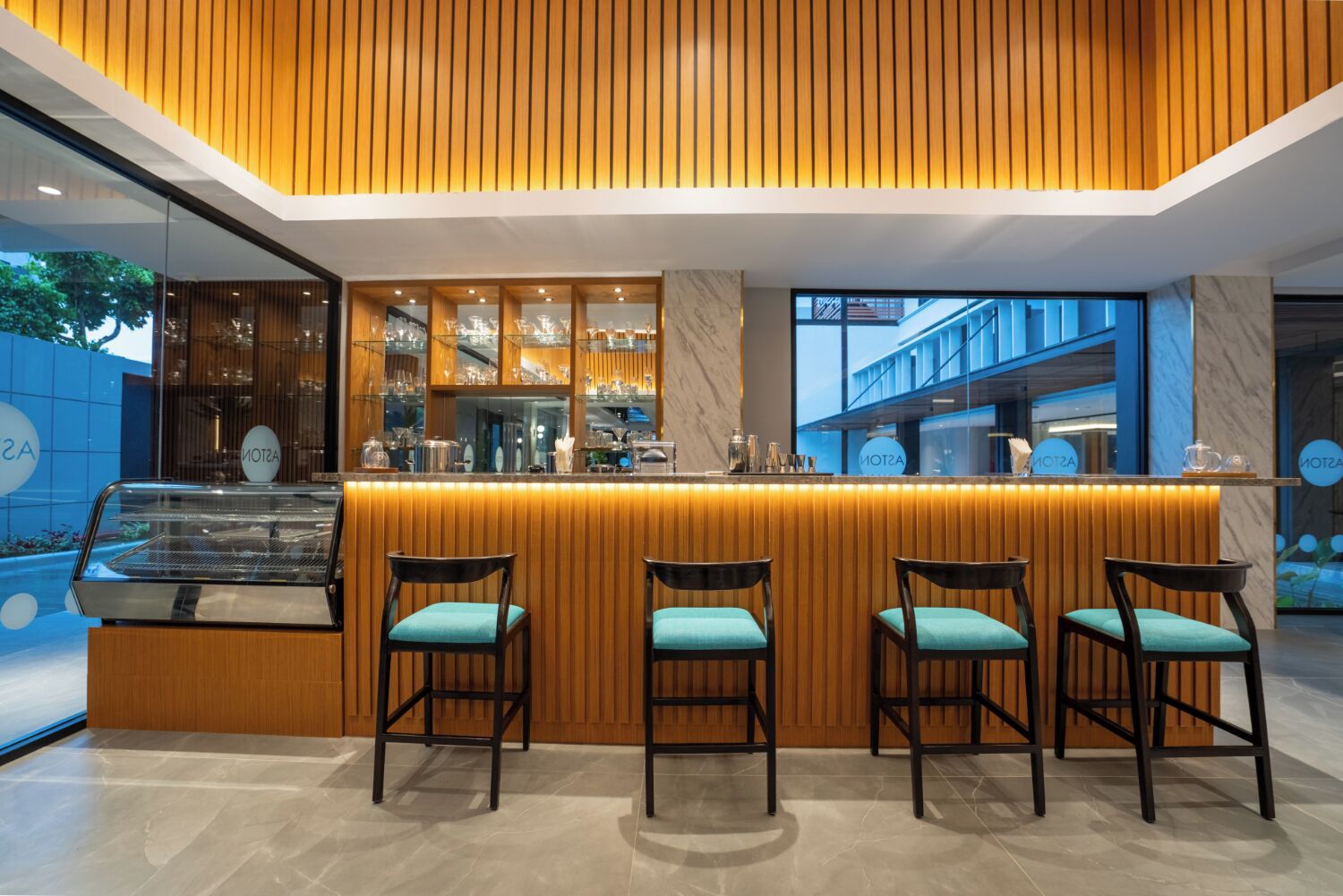 A modern bar area with wooden paneling, a marble countertop, and four bar stools with teal cushions.