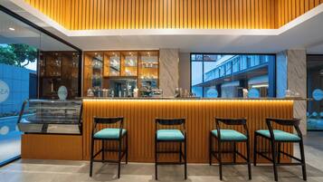 A modern bar area with wooden paneling, a marble countertop, and four bar stools with teal cushions.