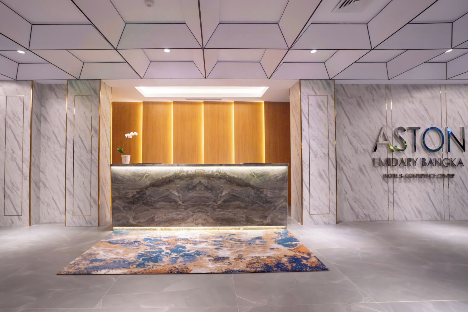 Un espace d’accueil doté d’un comptoir de réception en marbre, d’un grand tapis et d’une enseigne indiquant l’hôtel et centre de conférences ASTON Emidary Bangka.