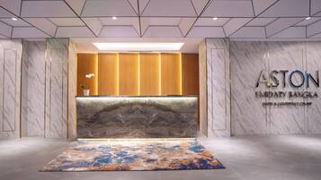 Un espace d’accueil doté d’un comptoir de réception en marbre, d’un grand tapis et d’une enseigne indiquant l’hôtel et centre de conférences ASTON Emidary Bangka.