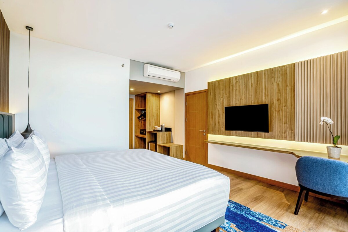 Une chambre d’hôtel moderne équipée d’un lit, d’un bureau, d’une chaise, d’un téléviseur fixé au mur et d’un appareil de climatisation.