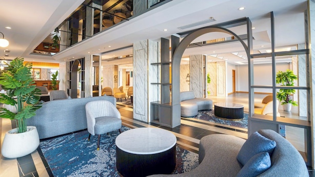 Eine moderne Hotelhalle mit hoher Decke, Marmorwänden und verschiedenen Sitzbereichen, darunter Sofas und Sessel.