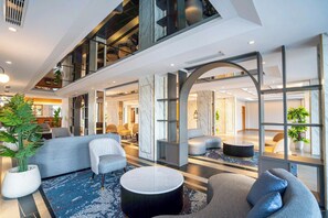 A modern hotel lobby with a high ceiling, marble walls, and a mix of seating areas including sofas and armchairs. - Aston Emidary Bangka Hotel And Conference Center (Pangkalpinang)