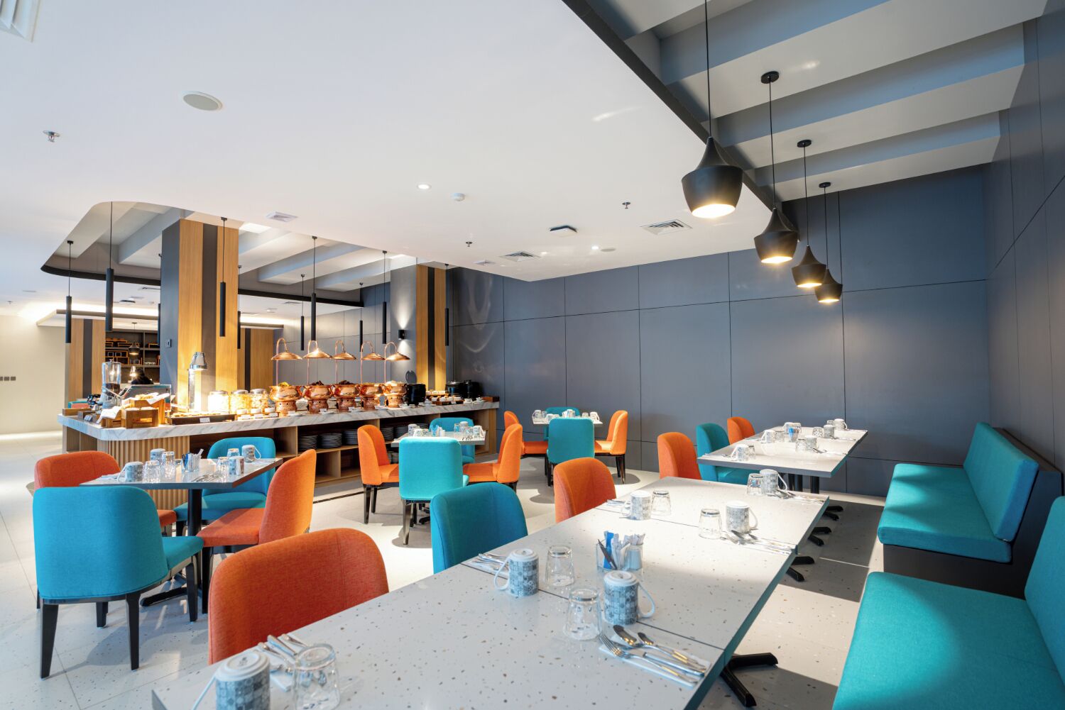 Un restaurante moderno con sillas de color naranja brillante y azul, una zona de bar central y un diseño limpio y contemporáneo.