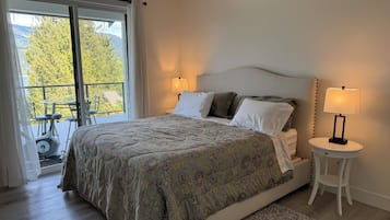 A bedroom with a bed, two bedside lamps, a small round table, and a view of a balcony with outdoor furniture.