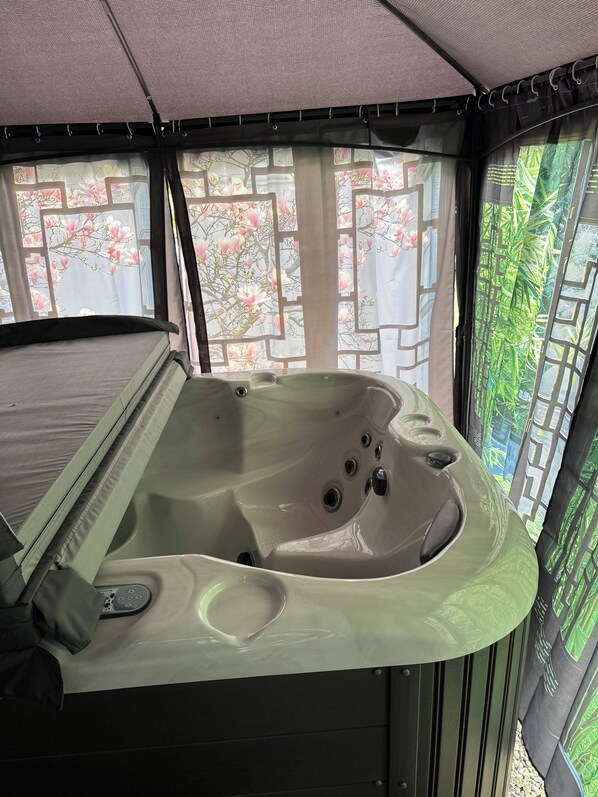 Un bain à remous au design incurvé, doté d’un panneau de commande et d’une fenêtre agrémentée de rideaux à motifs floraux.