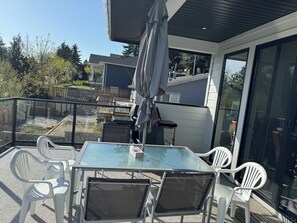 Un balcon fermé par des baies vitrées, avec une table et des chaises, un parasol et une vue sur les maisons voisines.