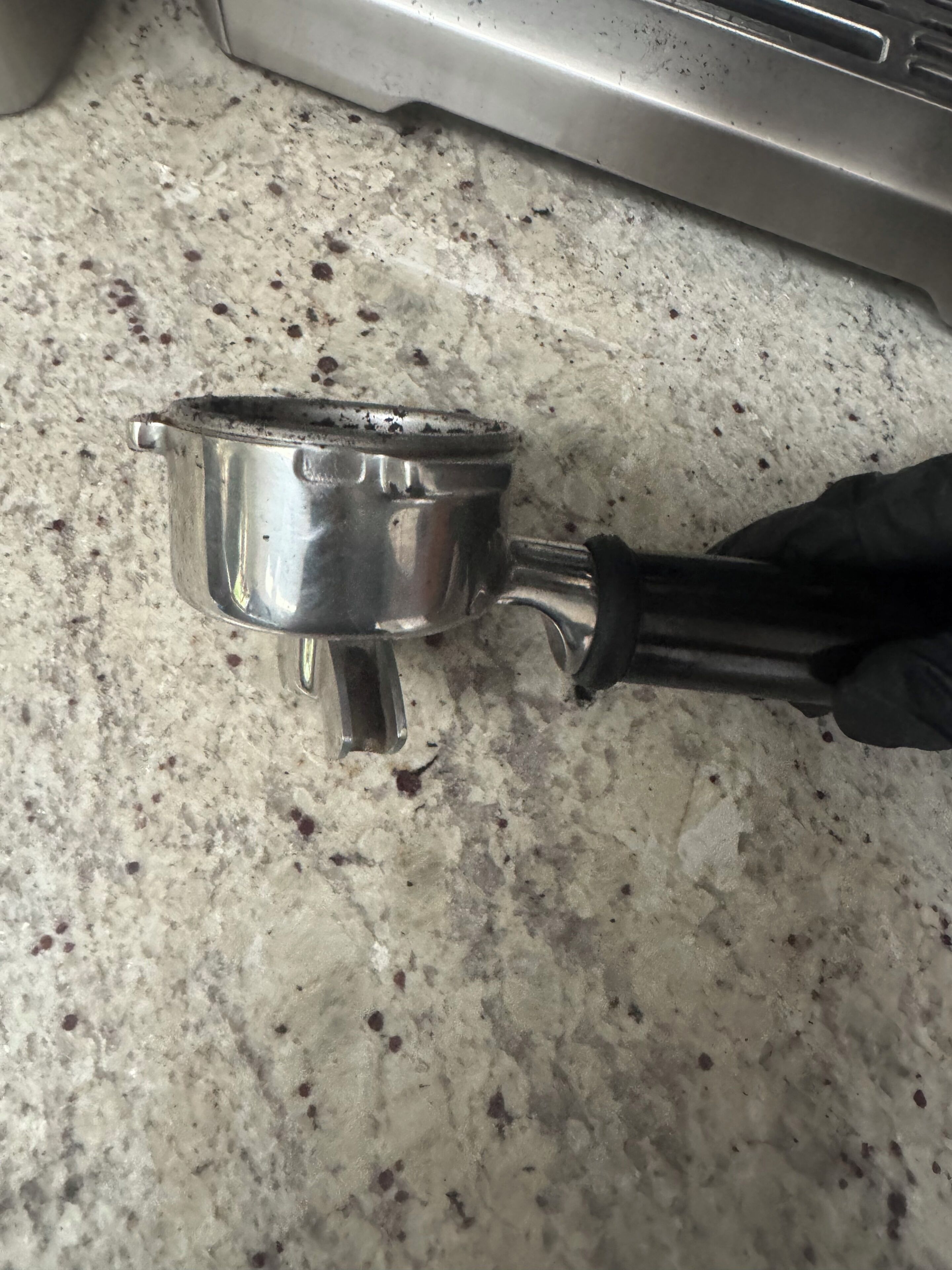 A metallic object with a black handle on a speckled surface.