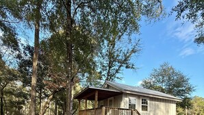 A single-story wooden cabin with a porch, surrounded by trees and a leaf-covered ground. - Comfy Standard Cabin (Andalusia)