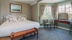 A bedroom with a large bed, a desk, a chair, and a window with curtains.