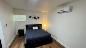 Une chambre à coucher comprenant un lit, une table de chevet, un climatiseur fixé au mur et un élément décoratif mural.