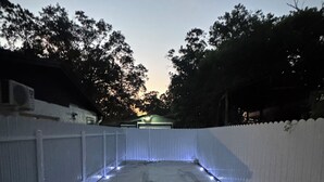 Un espace extérieur abrité, doté d’un sol en béton et d’une clôture blanche.