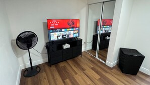 Une pièce équipée d’un téléviseur diffusant un film, d’un ventilateur, d’un meuble de rangement noir et d’un miroir.