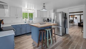 A modern kitchen with white cabinets, a stainless steel refrigerator, and a wooden island with stools.
