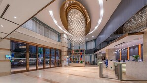 Un hall d’entrée spacieux, agrémenté d’un grand lustre central, d’un comptoir de réception et d’une façade vitrée.