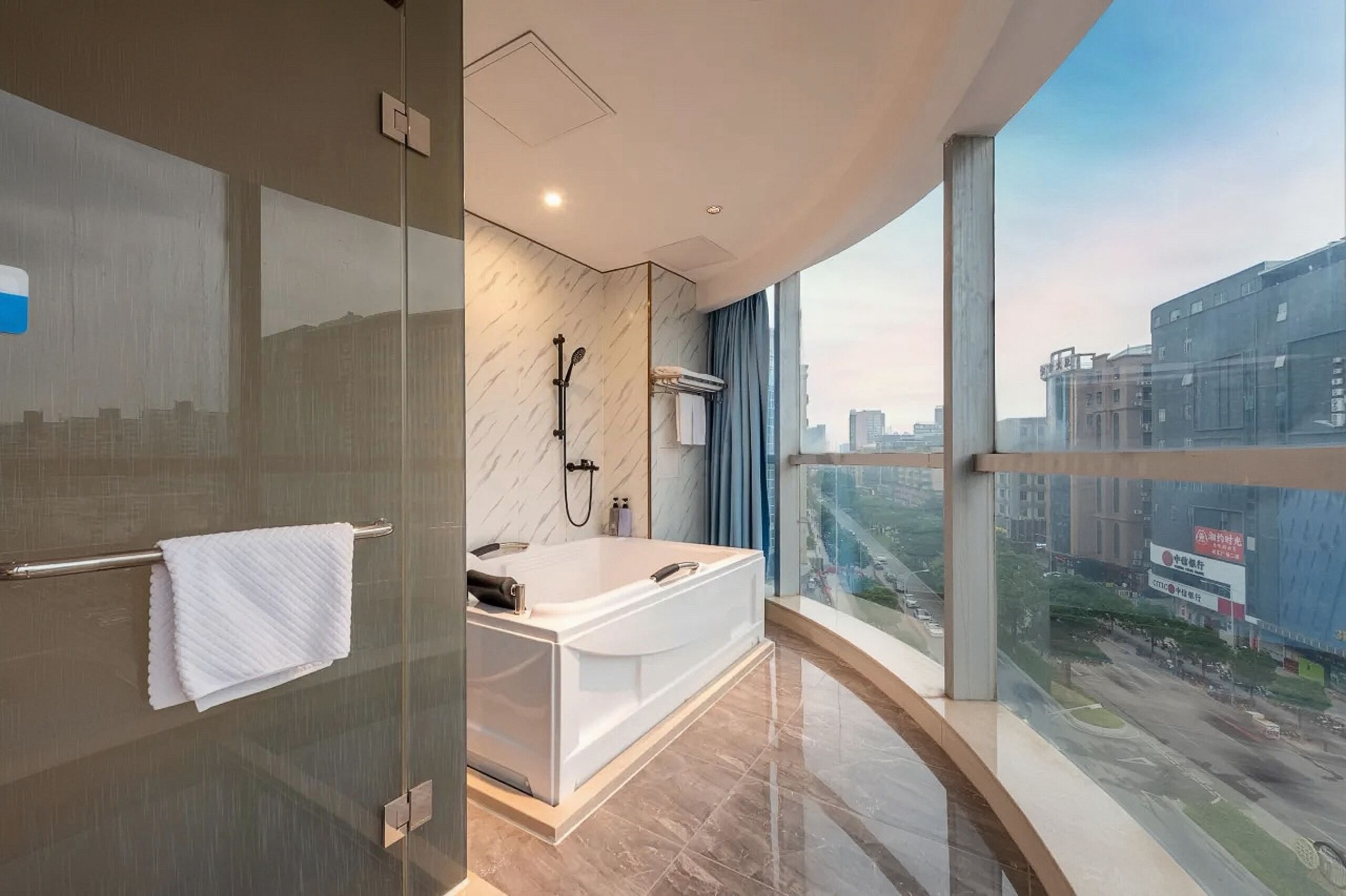A modern bathroom with a bathtub, a glass shower enclosure, and a large window offering a city view.