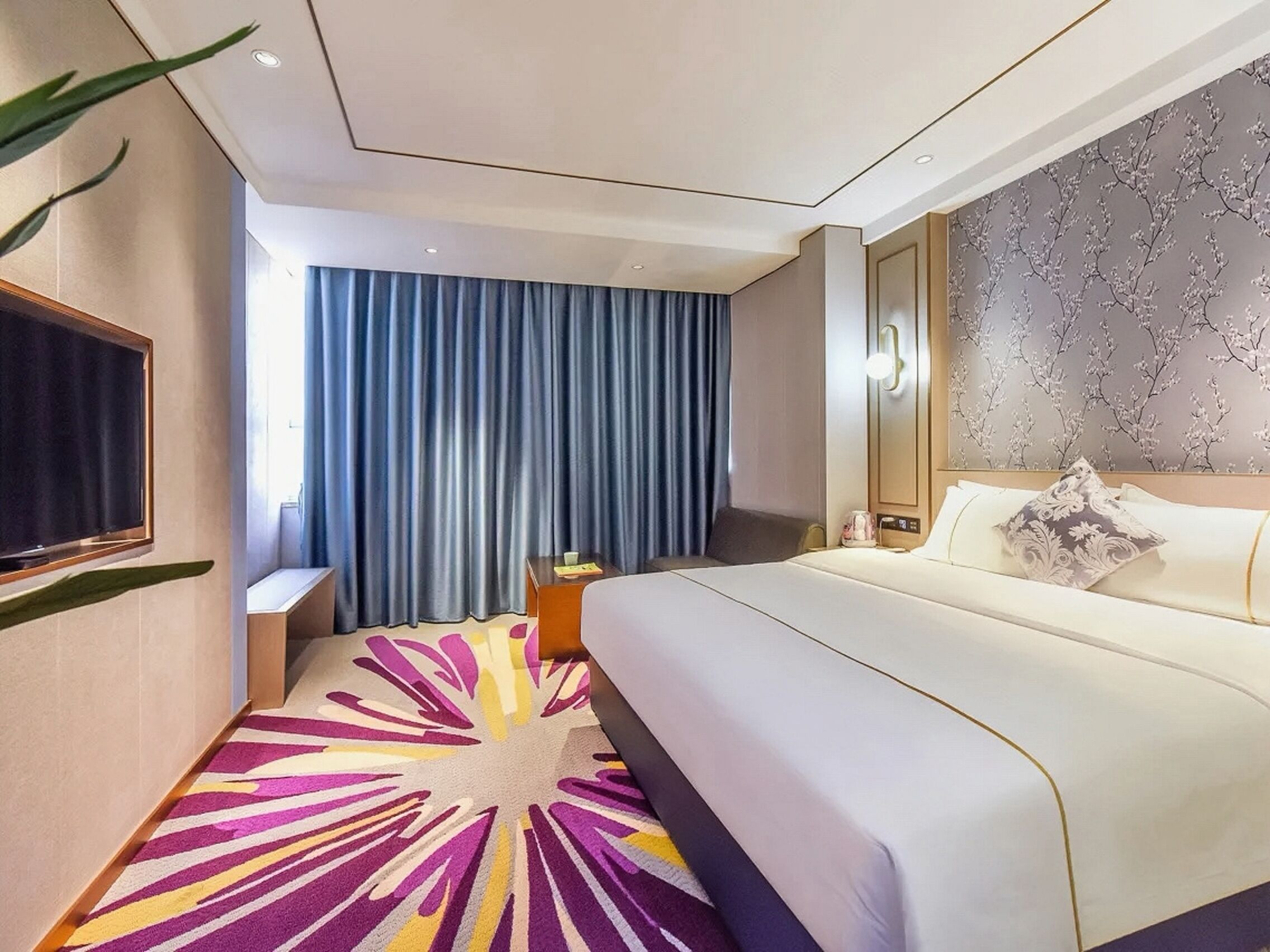 Ein Hotelzimmer mit Bett, Fernseher, Schreibtisch und einem fensterbepflanzten Fenster.