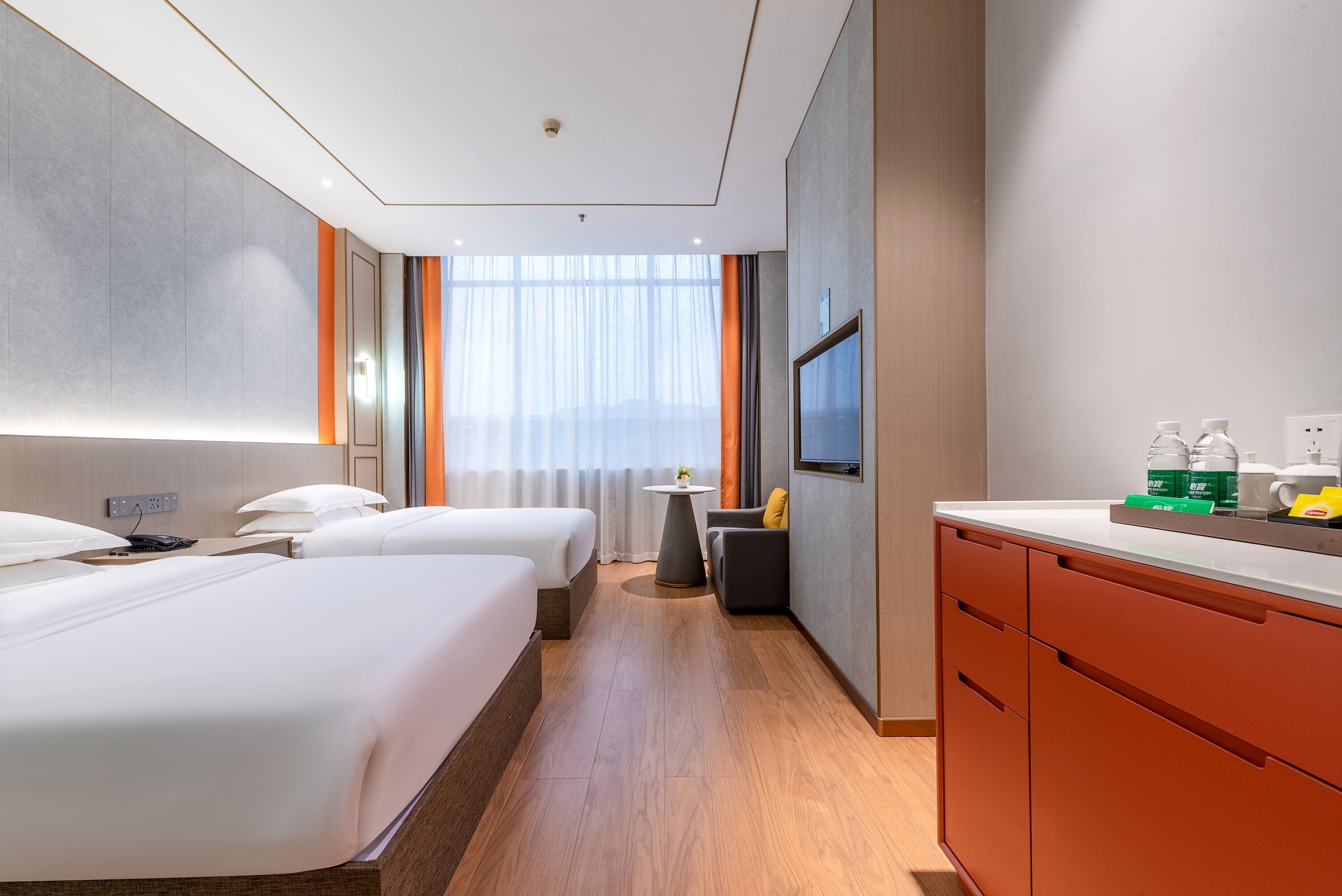 A hotel room with two beds, a small table, a TV, and a minibar.
