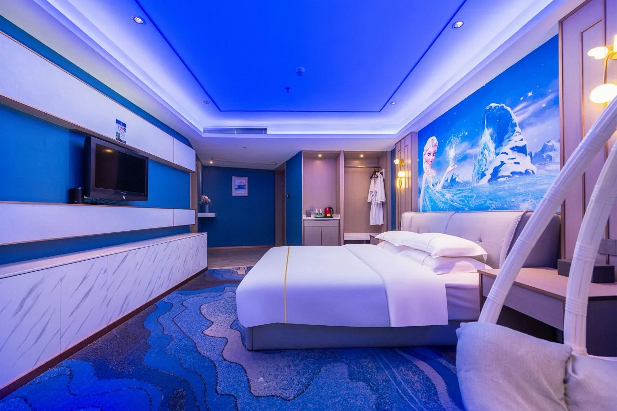 A modern hotel room with a large bed, a television, a bathroom with a shower, and a mural of a snowy landscape.